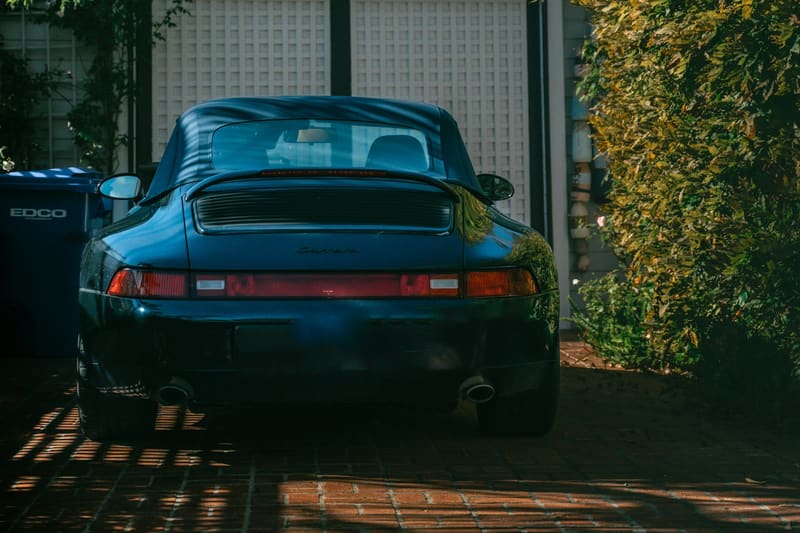 A dark blue Porsche 993 cabriolet, rear view, on a brick driveway in low evening sun.