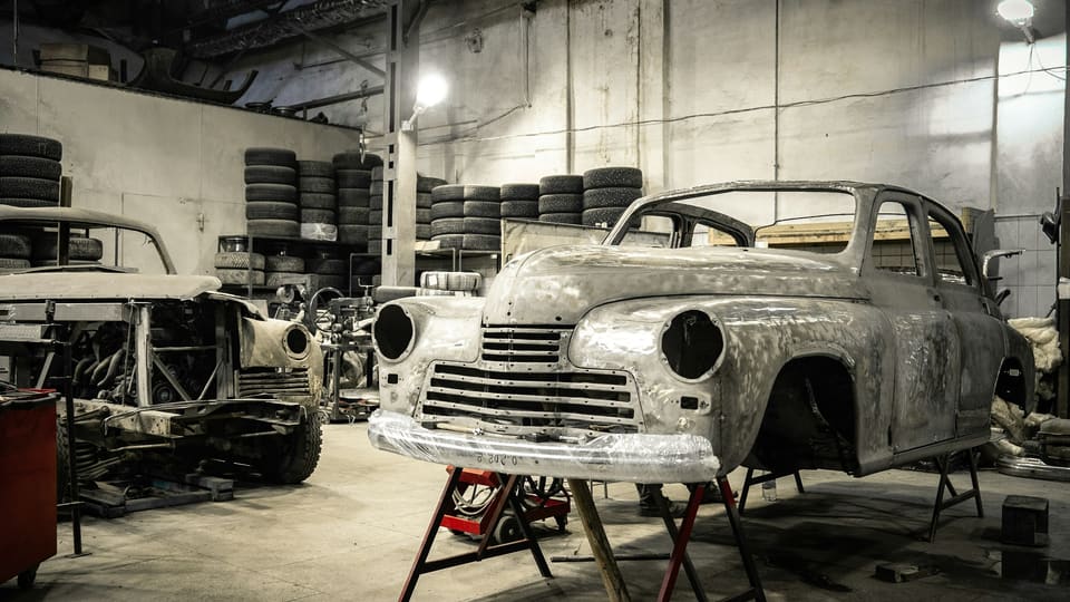 A bare-metal classic sedan body on stands mid-restoration, with tires racked behind it.