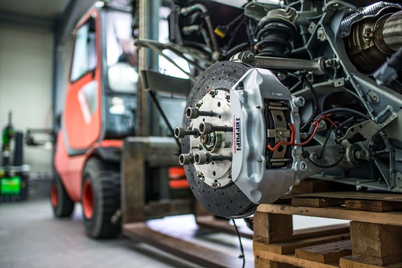 A drilled rotor and caliper assembly on a pallet in a bright shop.