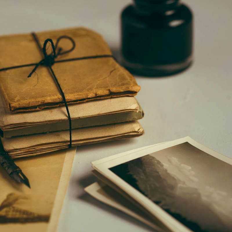 A tied bundle of aged papers with a dip pen, an ink bottle, and loose photographs on a pale surface.