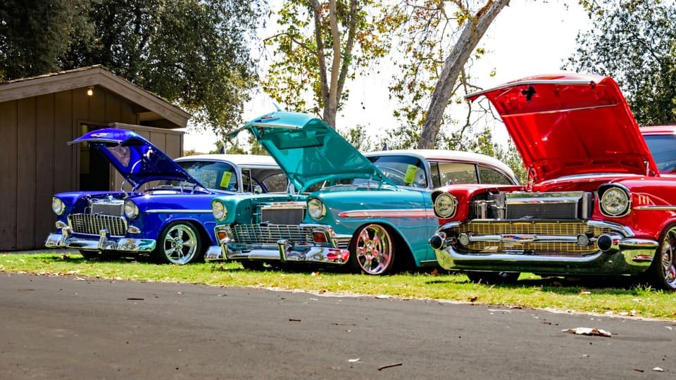 Three 1950s Chevrolets with their hoods raised, parked on a lawn at a daytime show.