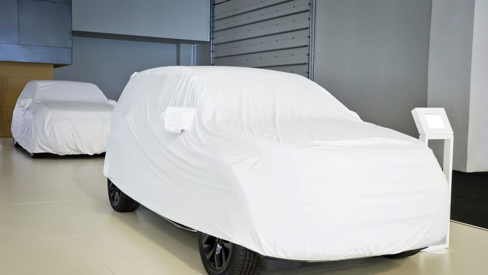 Two cars under fitted white covers in a bright, empty storage room.