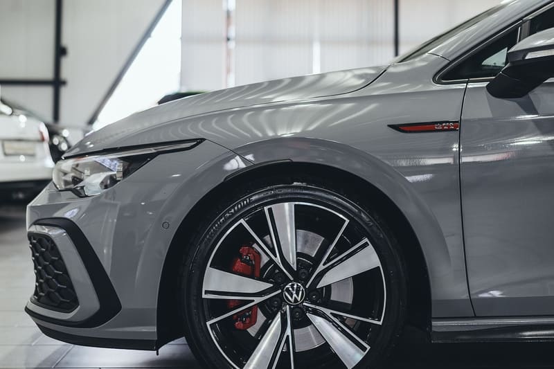 The front wheel and red brake caliper of a silver Volkswagen Golf GTI on a polished showroom floor.