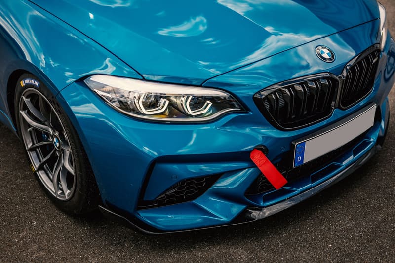The front quarter of a bright blue BMW M2 Competition, close on the headlight, kidney grille, and carbon front splitter.