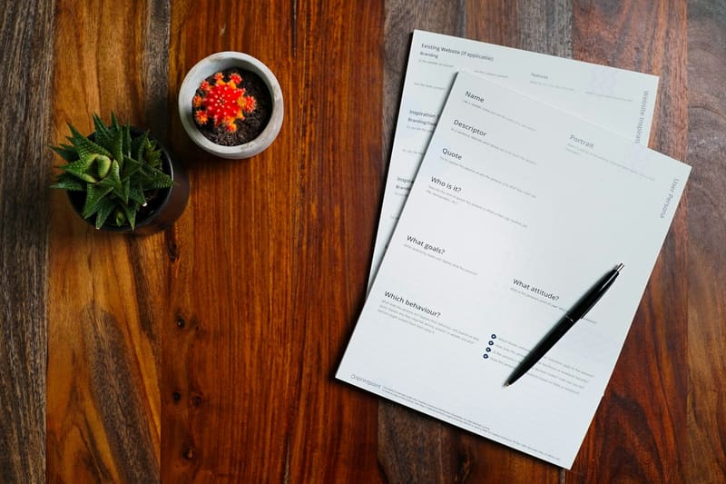 Printed forms and a pen on a walnut desk.