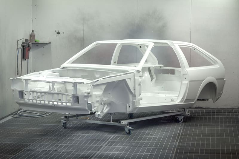 A primered body shell on a dolly in a clean spray booth.