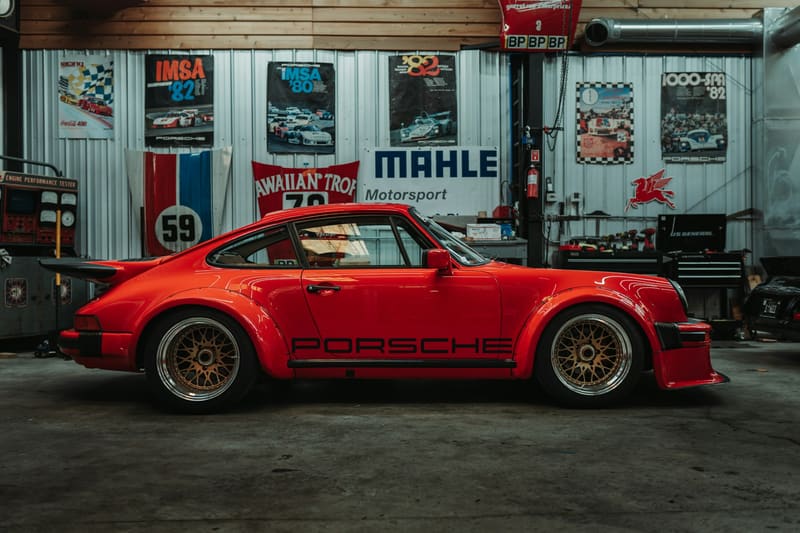 A red 1980s Porsche 930 Turbo in side profile inside a tidy shop hung with motorsport posters.