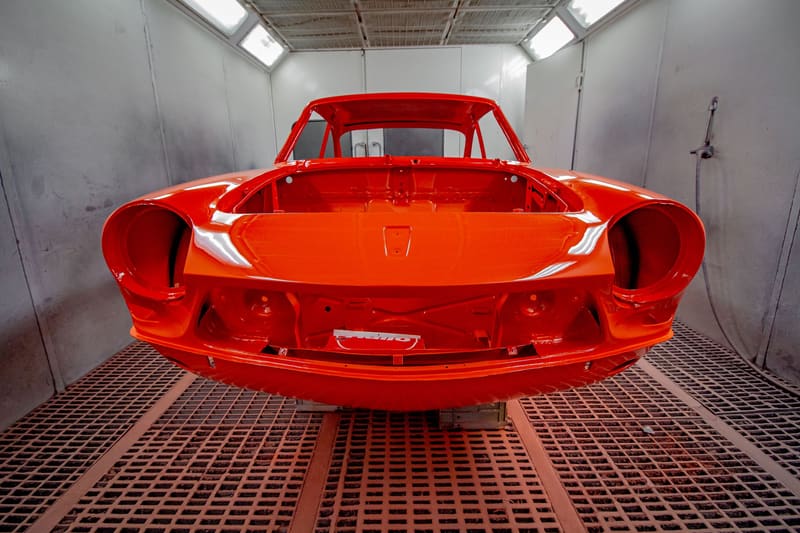 A freshly painted red sports-car body shell alone in a clean spray booth.