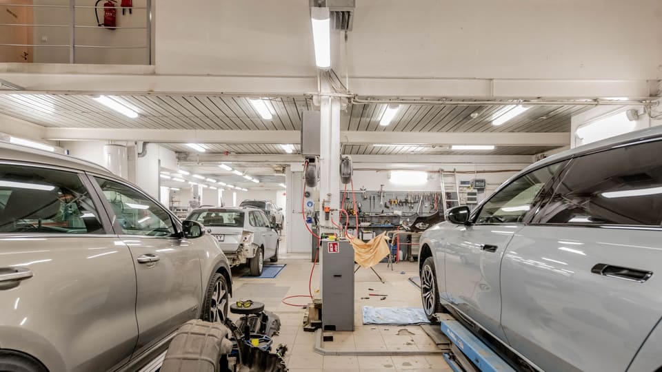 Two cars with their wheels off in adjacent bays of a tidy shop under overhead strip lighting.