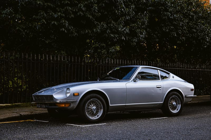A silver coupe in side three-quarter view in daylight, against a dark hedge.