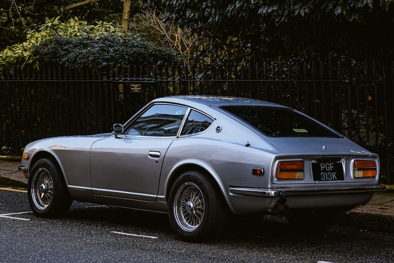 A silver coupe photographed from the side in daylight, behind a park railing.