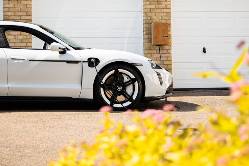 A white electric sedan on charge outside a brick home garage with white doors.