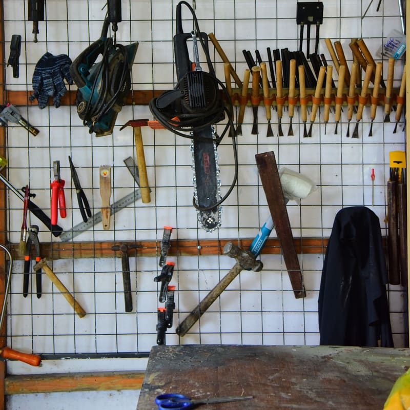 A white wire-grid tool wall with hand tools hung in ordered rows above a clean bench.