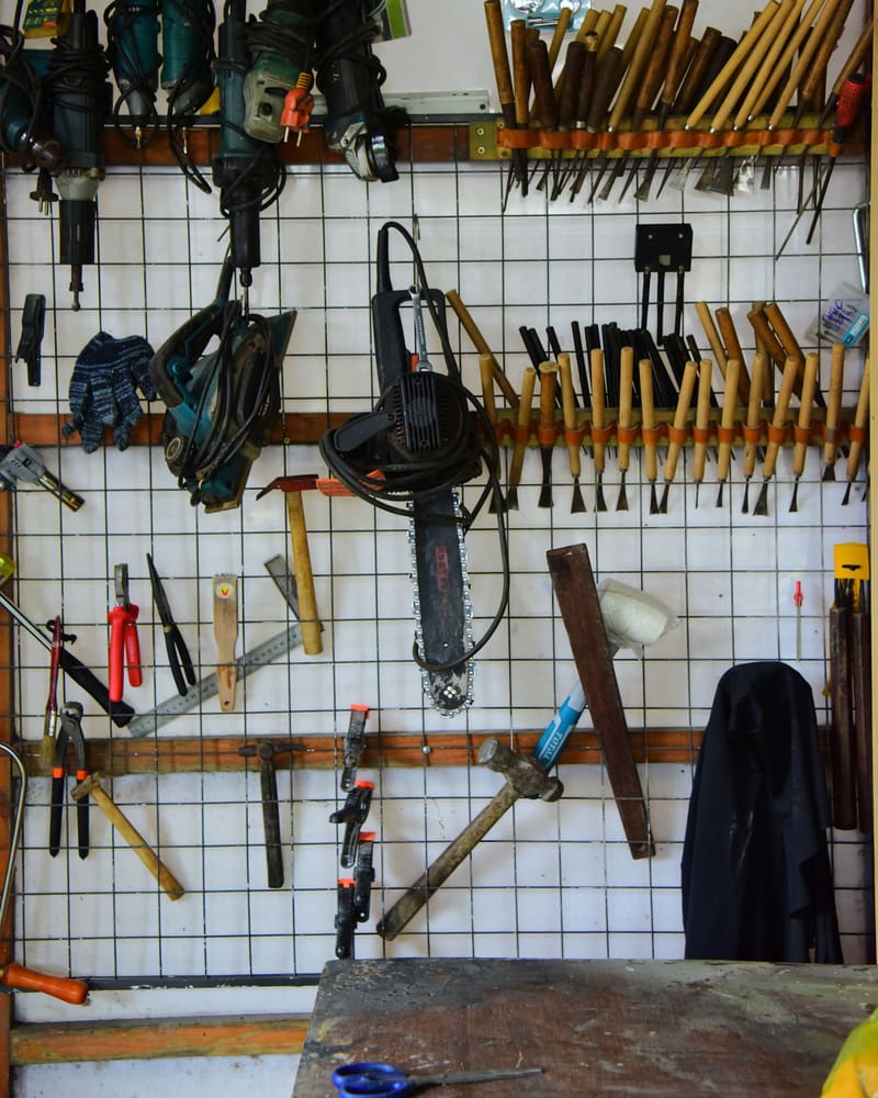 A white wire-grid tool wall with hammers, chisels and pliers hung in ordered rows.