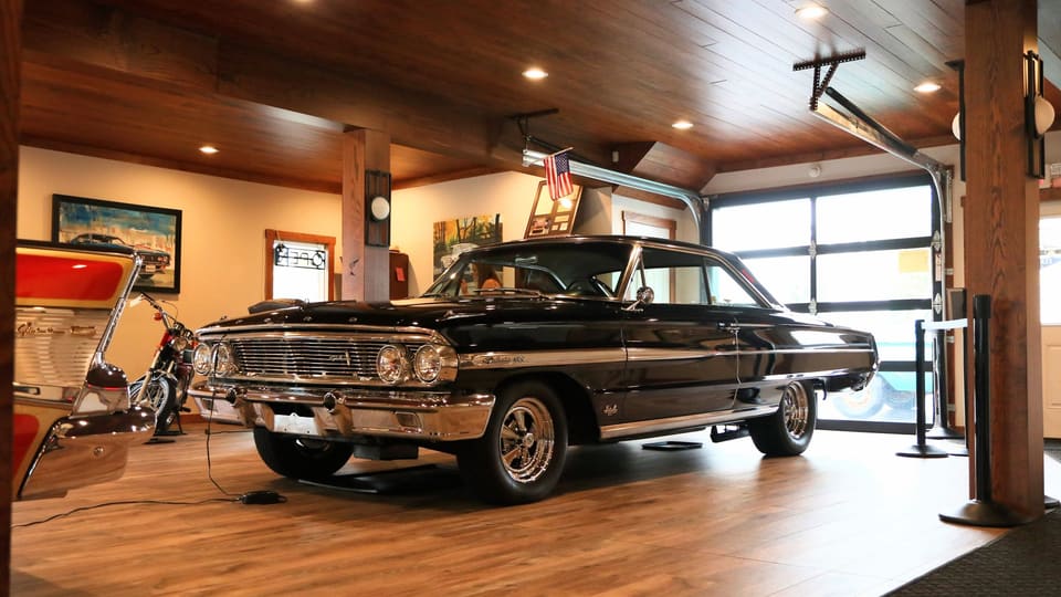 A black 1960s coupe in a wood-lined, lamp-lit private garage.