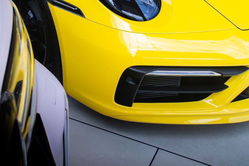 The hood and headlight of a yellow current-shape Porsche 911 on a pale showroom floor.